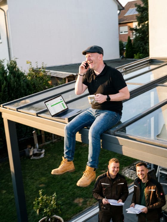 Betriebsinhaber am Telefon, während das Team auf der Baustelle arbeitet